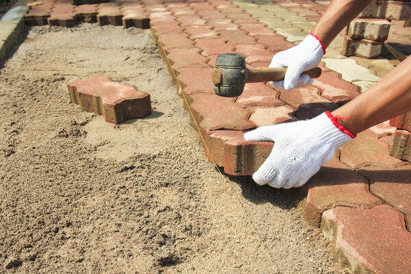 Worker laying red concrete paving blocks.