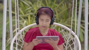 Orta yaşlı kadın salıncakta dinleniyor arka bahçedeki tablet bilgisayarda müzik dinliyor...