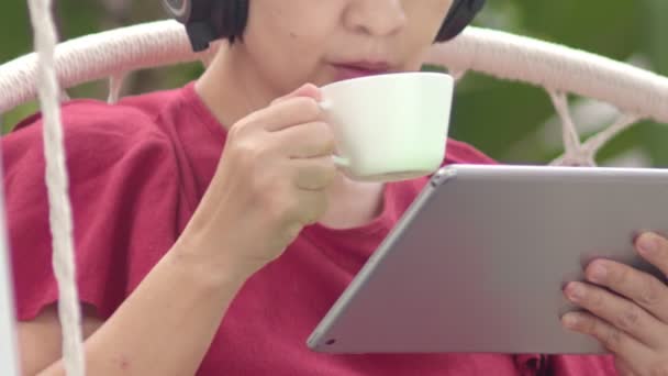 中年女性リラックスオンスイングリッスン音楽オンザタブレットコンピュータ上の裏庭 — ストック動画