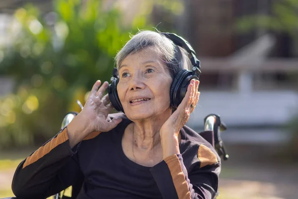 亚洲老年妇女在后院用耳机听音乐 — 图库照片