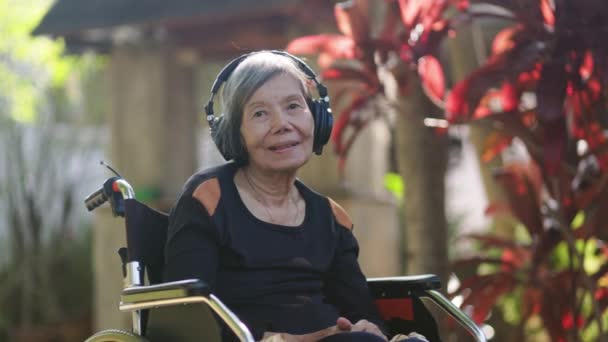 Ασιάτισσα Ηλικιωμένη Γυναίκα Ακούει Μουσική Ακουστικά Στην Πίσω Αυλή — Αρχείο Βίντεο