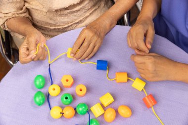 Bakıcı ve yaşlı kadın bunamayı önlemek için boncuk dizme oyunu oynuyorlar.