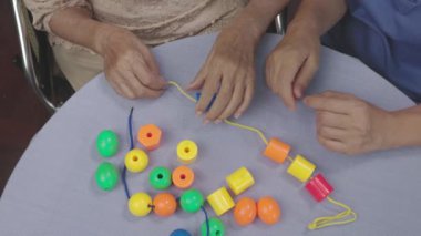 Bakıcı ve yaşlı kadın bunamayı önlemek için boncuk dizme oyunu oynuyorlar.