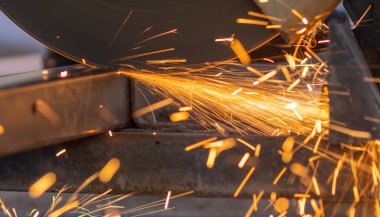 Worker cutting steel rectangular pipe in construction site.