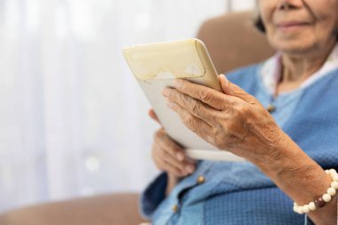 Oturma odasındaki eski tablette internette gezinen yaşlı bir kadın..