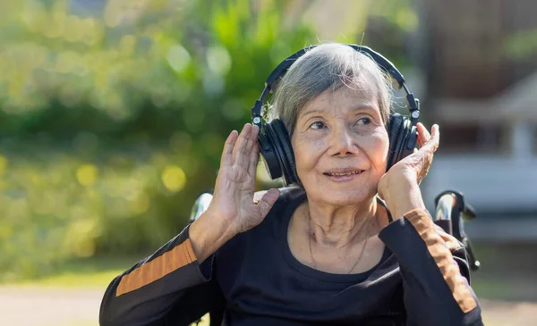 Asiática Senior Mujer Escuchando Música Con Auriculares Patio Trasero Imagen de stock