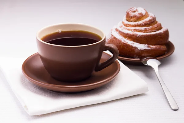 Taza de té negro en servilleta blanca con bollo dulce — Foto de Stock