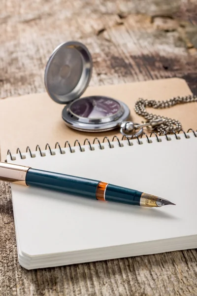 Golden in pen with pocket watch at white notebook — Stock Photo, Image