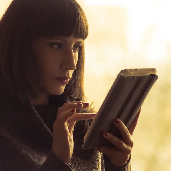 Mujer bonita joven usando Tablet Computer cerca de la ventana. Imagen tonificada de color cálido — Foto de Stock