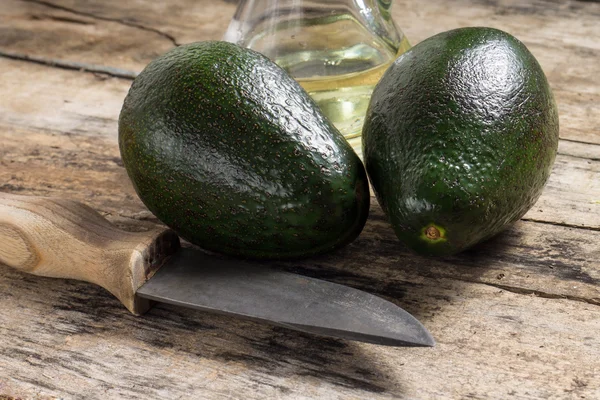 Two avocado with Knife and Bottle of Oil on Wood Background — Stock Photo, Image