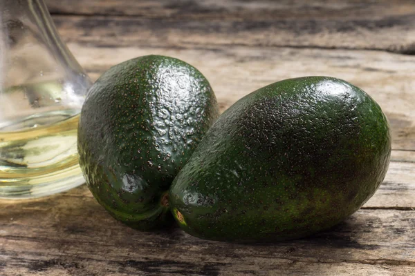 Two Raw Avocado with Bottle of Oil on Grunge Wood Background — Stock Photo, Image