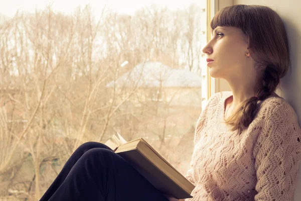 Joven chica adulta leyendo libro cerca de la ventana — Foto de Stock