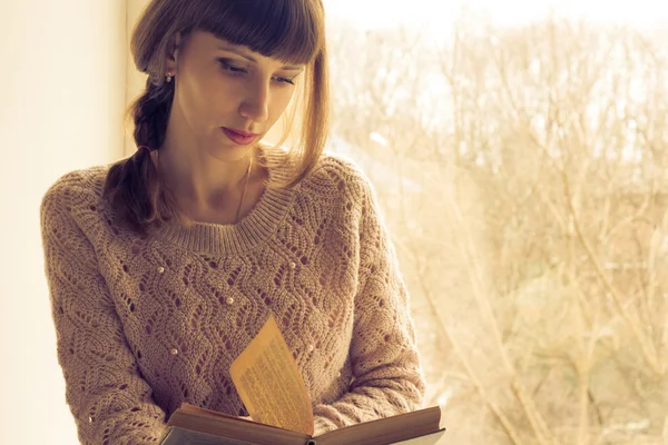 Pencerenin yanında kitap okuyan genç bir kız. — Stok fotoğraf