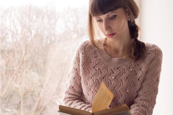 Jovencita leyendo libro cerca de la ventana . — Foto de Stock