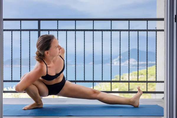 Genç jimnastikçi kadın deniz kenarındaki balkonda yoga yapıyor. — Stok fotoğraf
