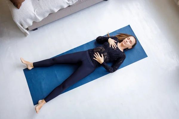 Молода струнка красива жінка лежить на килимку в позі Шавасана йоги — стокове фото