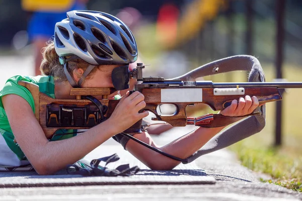 Young girl aiming her rifle on biathlon shooting range. Summer biathlon competition image with unrecognizable athlete