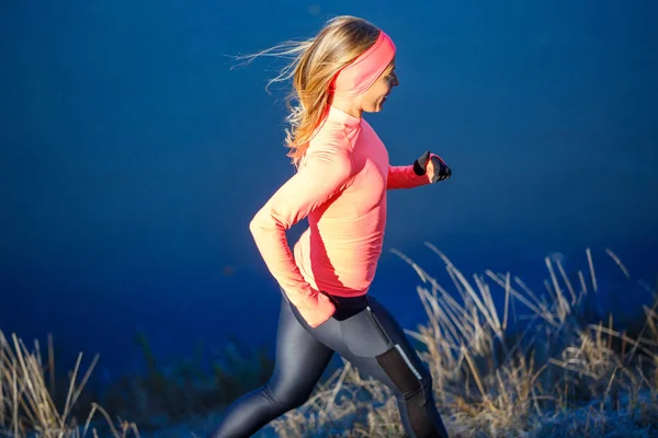 Молодая спортивная женщина в оранжевом длинном рукаве бежит по синему ледяному озеру утром — стоковое фото