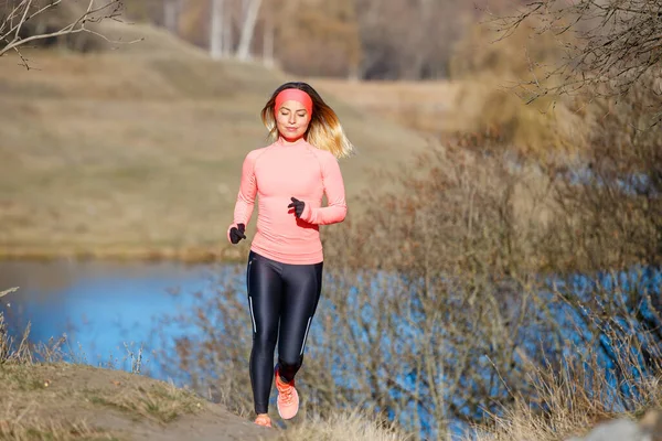 Jonge vrouw joggen in het park bij de vijver in de koude zonnige ochtend — Stockfoto