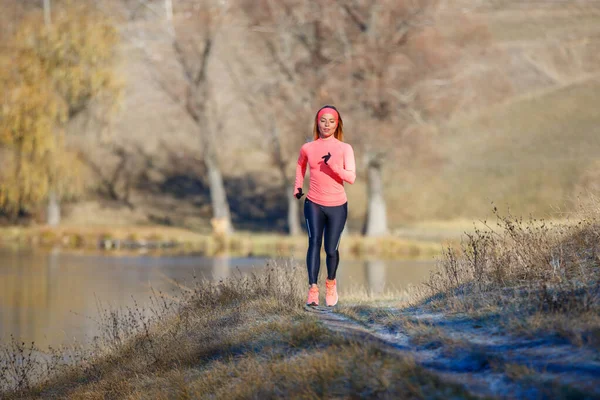 Fitness menina correndo no parque perto da lagoa na manhã gelada. — Fotografia de Stock