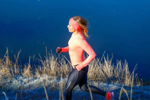 Fiatal sportos nő narancssárga hosszú ujjú fut végig kék fagyos tó reggel — Stock Fotó