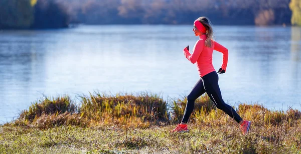 Young slim woman running along the lake in the cold morning — Stock Photo, Image