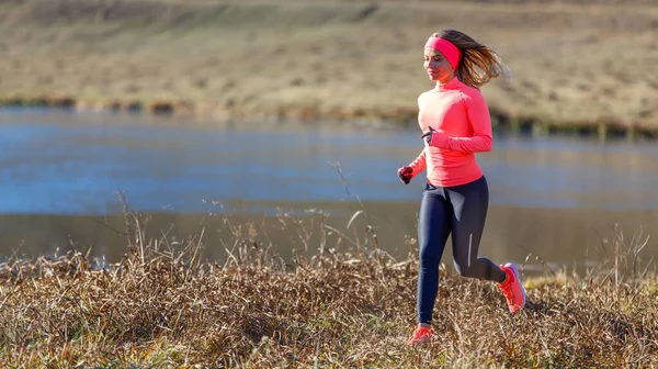 Giovane donna magra che corre lungo il lago al mattino freddo — Foto Stock