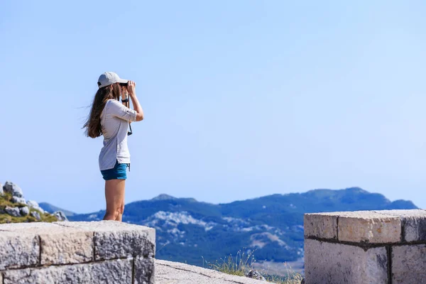 Young woman watching mountain landscape through binoculars at the view spot on tourist trail — Stok fotoğraf
