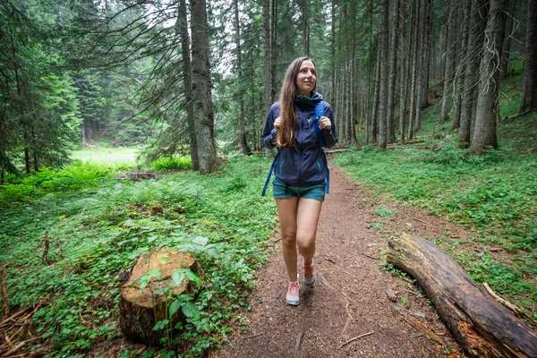 Jovem mulher sorridente com mochila andando no caminho da floresta — Fotografia de Stock