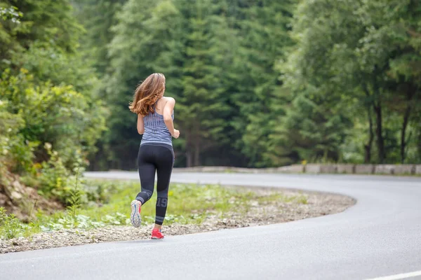 Fiatal fitnesz nő fut az úton keresztül az erdőben — Stock Fotó