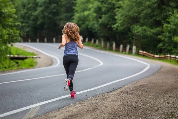 Young fitness woman running on the road through the forest — Stock Photo, Image