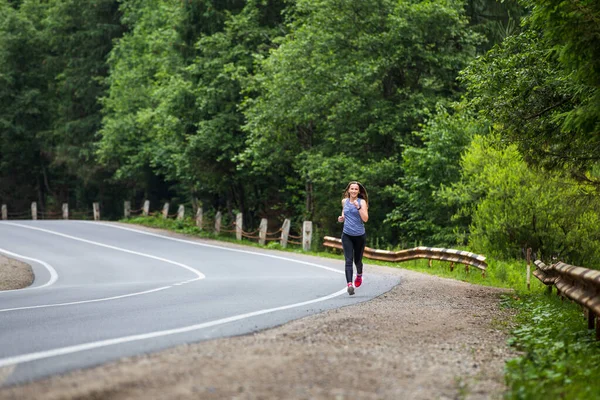 Runner woman running on the mountain road through the forest. — Stock Photo, Image