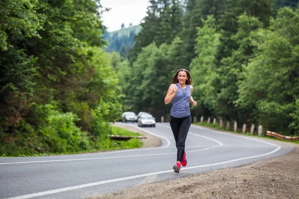 Futó nő fut a hegyi úton az erdőn keresztül. — Stock Fotó