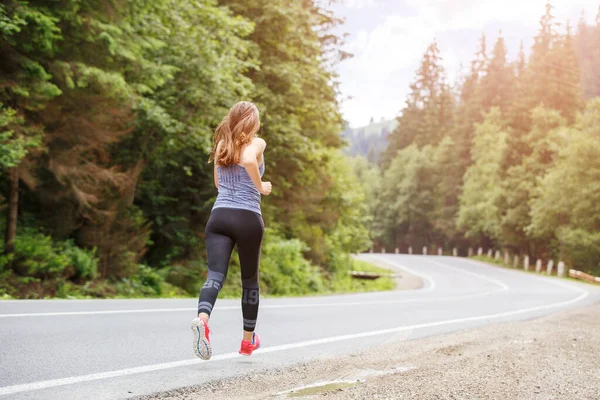 Young fitness woman running on the road through the forest — Stock Photo, Image