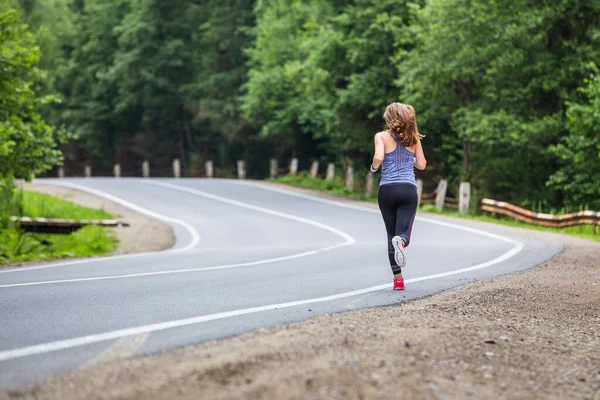 Young fitness woman running on the road through the forest — Stock Photo, Image