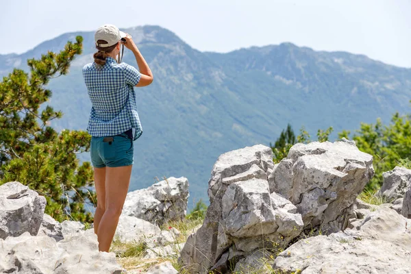 Ung kvinna tittar genom kikare på fågelskådning plats i bergen — Stockfoto