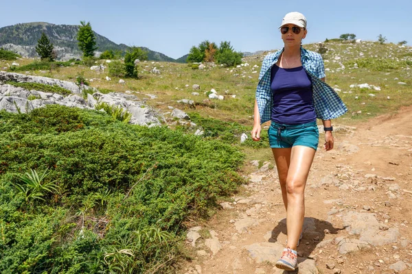 Jovem mulher caminhando pelo prado rochoso nas montanhas — Fotografia de Stock