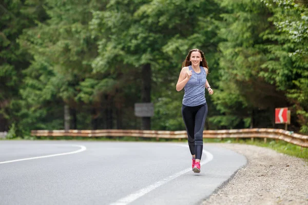 Fiatal fitnesz nő fut az úton keresztül az erdőben — Stock Fotó