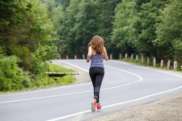 Young fitness woman running on the road through the forest — Stock Photo, Image