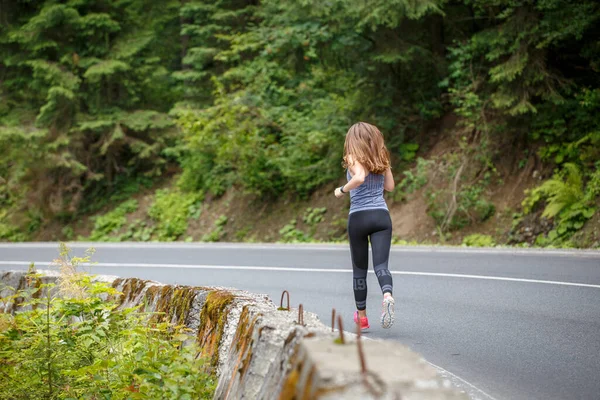 Jovem mulher fitness correndo na estrada através da floresta — Fotografia de Stock
