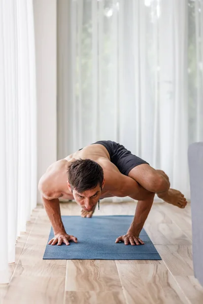 Young man doing strength pilates or yoga workout in the morning. Muscular man practicing sweat yoga at home