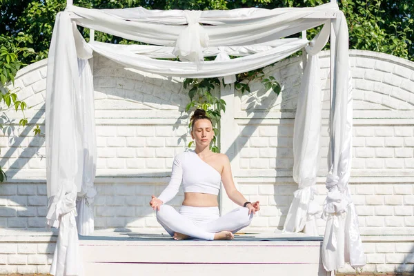 Young yoga woman in white sportswear meditating outdoor in the morning. Breathing yoga class