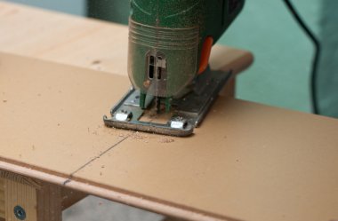 Close up image of an electric jigsaw cutting sheets on a wooden plank