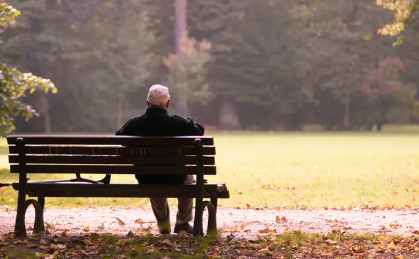 Viejo sentado en un banco en otoño, otoño de la vida Royalty Free Stock Fotografie