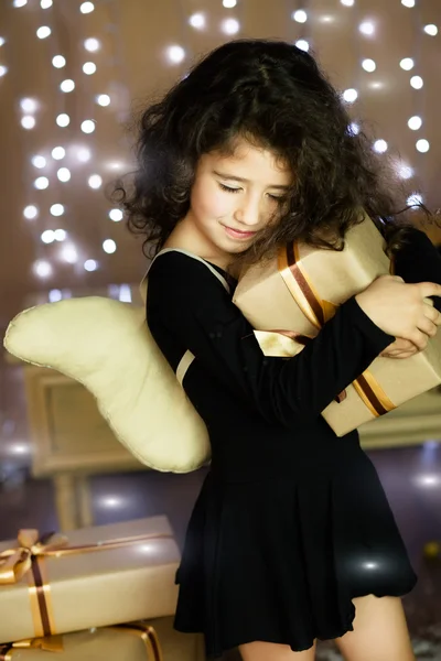 Menina encaracolado em traje de anjo segurando presente em suas mãos — Fotografia de Stock