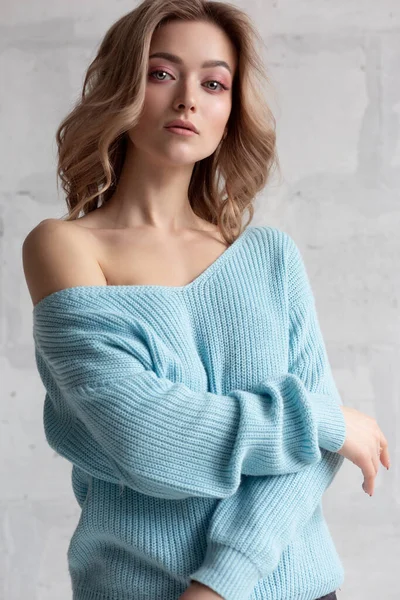 Sexy blonde girl in a blue knitted sweater on a white wall background — Stok fotoğraf