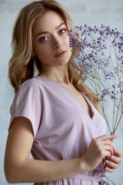 Beyaz bluzlu, elinde çiçekle çekici bir kadının portresi. Gri arkaplanda stüdyo fotoğrafı