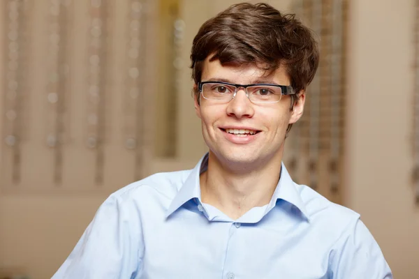 Young man at optician with glasses, background in optician shop — Stock Photo, Image