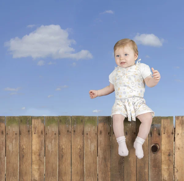 Babymeisje zittend op een hek — Stockfoto