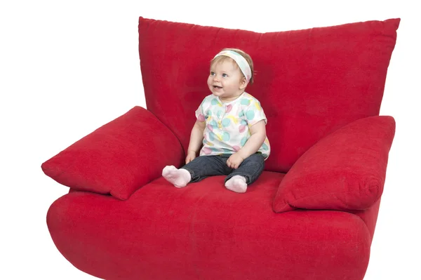 Bebê menina sentada em um grande sofá vermelho — Fotografia de Stock